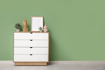 Modern dresser with figurine, houseplants and photo frames near green wall