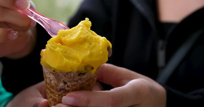 Close-up of eating mango ice cream with small plastic spoons