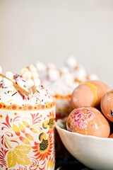 Composition of easter cake with protein glaze, sugar sprinkles, marshmallow on top and eggs decorated with patterns, on a with blurred background. Orthodox Easter in eastern Europe. Vertical photo