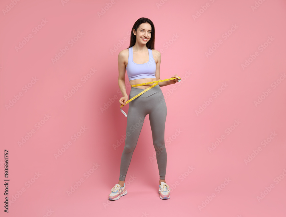 Poster Happy young woman with measuring tape showing her slim body on pink background