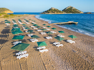 Aerial view of empty sandy beach with sun beds and green umbrellas, beautiful sea and green hills...