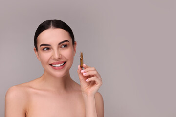 Beautiful young woman holding skincare ampoule on grey background. Space for text