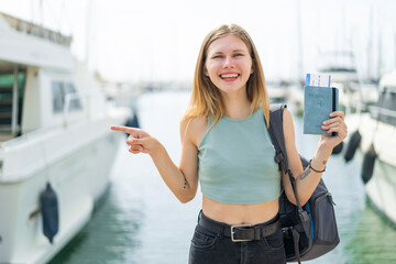 Young blonde woman holding a passport at outdoors surprised and pointing finger to the side