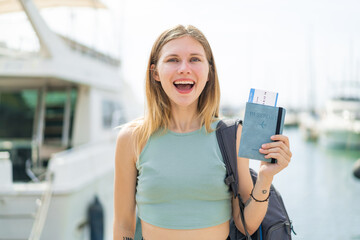 Young blonde woman holding a passport at outdoors with surprise and shocked facial expression