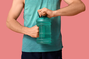 Sporty guy opening bottle of water on pink background, closeup