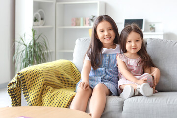 Obraz premium Cute little Asian happy sisters sitting on sofa at home