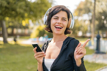 Young pretty Bulgarian woman at outdoors listening music with a mobile and singing