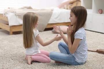Cute little sisters playing clapping game with hands at home