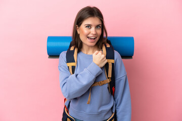 Young mountaineer woman with a big backpack isolated on pink background celebrating a victory