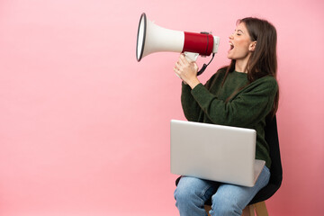 Young caucasian woman sitting on a chair with her laptop isolated on pink background shouting...