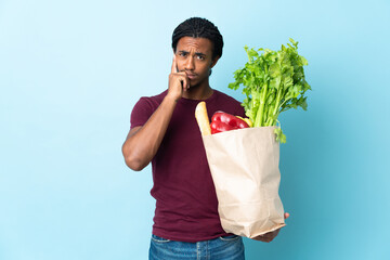 African American man holding a grocery shopping bag isolated on blue background thinking an idea