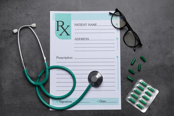 Medical prescription form, stethoscope, pills and glasses on dark grey table, flat lay