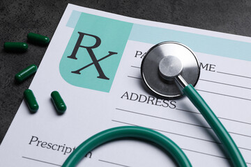 Medical prescription form, stethoscope and pills on dark grey table, closeup