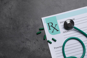 Medical prescription form, stethoscope and pills on dark grey table, flat lay. Space for text