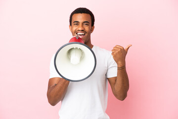 African American handsome man on isolated pink background shouting through a megaphone and pointing...