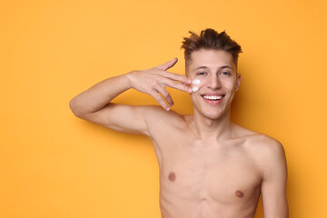 Handsome man applying moisturizing cream onto his face on orange background. Space for text