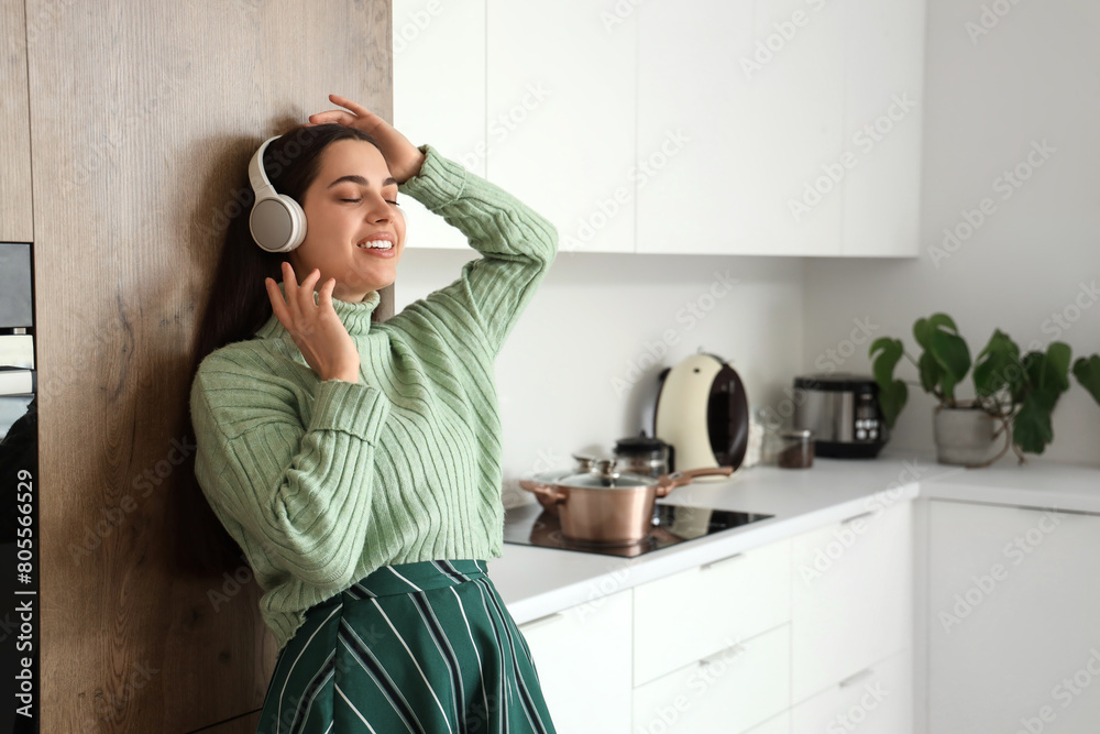 Canvas Prints Beautiful young happy woman in headphones listening music at kitchen