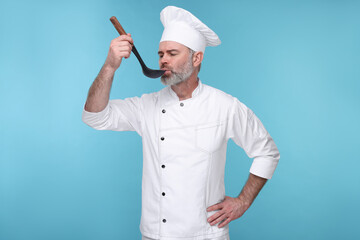 Chef in uniform tasting something on light blue background