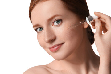 Fototapeta premium Beautiful woman with freckles applying cosmetic serum onto her face on white background