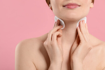 Woman with freckles wiping neck on pink background, closeup