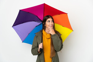 Young woman holding an umbrella isolated on white background looking up while smiling