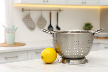 Empty colander and fresh lemon on white marble table in kitchen. Space for text