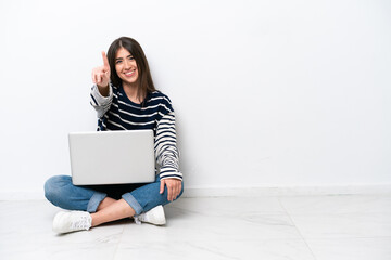 Young caucasian woman with a laptop sitting on the floor isolated on white background showing and lifting a finger