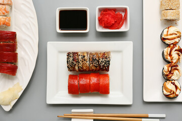 Tasty sushi rolls with chopsticks, marinated ginger and soy sauce on grey background