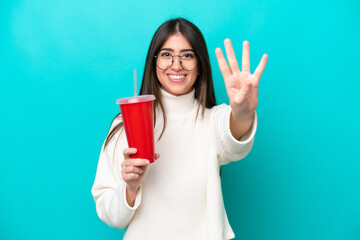 Young caucasian woman drinking soda isolated on blue background happy and counting four with fingers