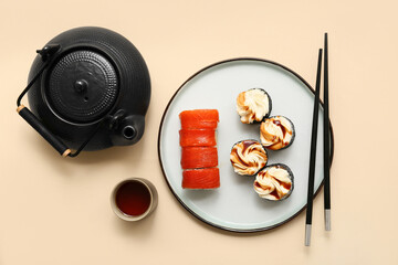 Tasty sushi rolls with chopsticks, teapot and cup of tea on beige background - Powered by Adobe