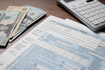 Payroll. Tax return forms, dollar banknotes and calculator on wooden table