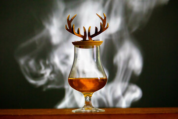 Single malt scotch whiskey in crystal glass with deer antler and smoke rustic background