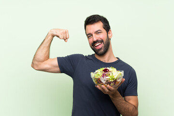 Young handsome man with salad over isolated green wall doing strong gesture