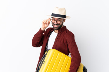 Traveler man man with beard holding a suitcase over isolated white background with glasses and smiling