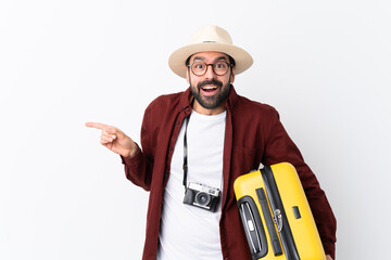 Traveler man man with beard holding a suitcase over isolated white background surprised and pointing finger to the side