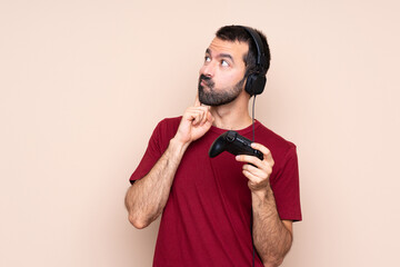 Man playing with a video game controller over isolated wall thinking an idea while looking up
