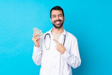 Young caucasian man over isolated background wearing a doctor gown and holding pills