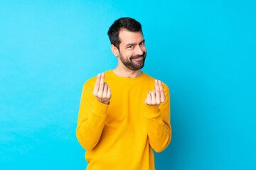 Young caucasian man over isolated blue background making money gesture