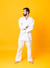 Full-length shot of man over isolated yellow background doing karate keeping the arms crossed