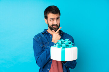 Young handsome man with a big cake over isolated blue background thinking