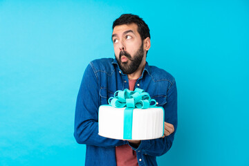 Young handsome man with a big cake over isolated blue background making doubts gesture while lifting the shoulders
