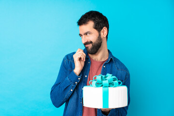 Young handsome man with a big cake over isolated blue background scheming something