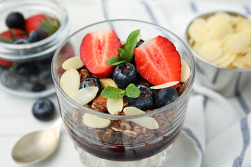 Tasty granola with berries, jam and almond flakes in glass on white table, closeup