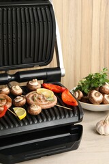 Electric grill with homemade sausages, mushrooms and bell pepper on wooden table