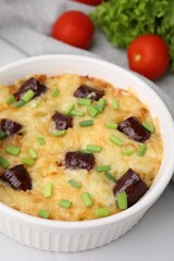 Tasty sausage casserole with green onions in baking dish served on white tiled table, closeup