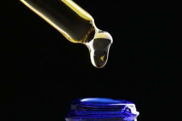 Dripping tincture from pipette into bottle on black background, closeup