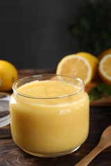Delicious lemon curd in glass jar, fresh citrus fruits and spoon on wooden table