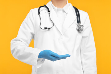 Doctor with stethoscope holding something on orange background, closeup