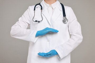 Doctor with stethoscope holding something on grey background, closeup