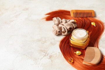 Red strand with jar of hair mask, combs and scrunchy on beige grunge background, closeup